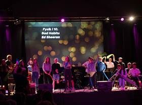 Gruppe af mennesker på scenen, skærm med teksten 