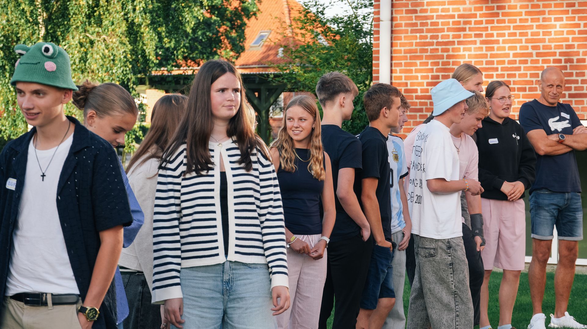 Gruppe af mennesker, der griner og taler på en græsmark foran en bygning i sollyset.
