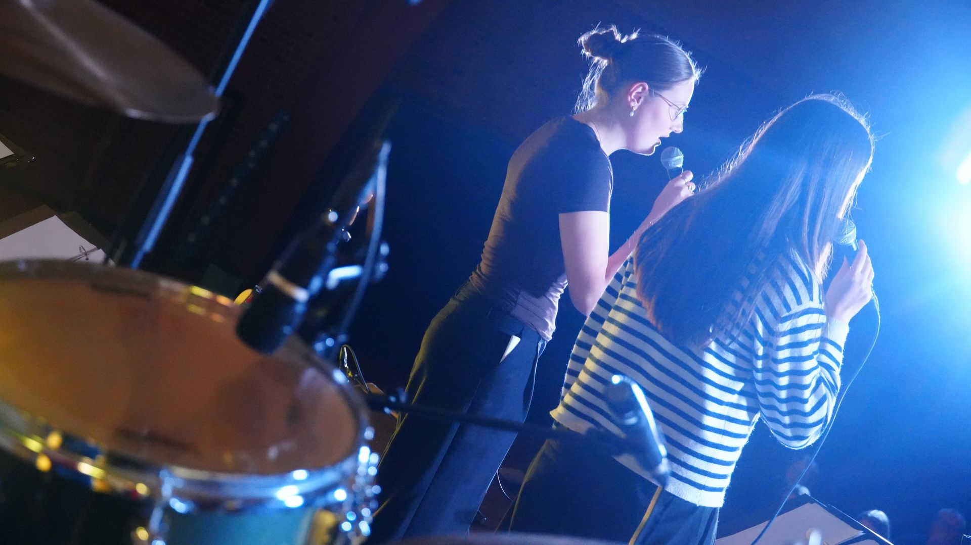 Koncertpublikum med løftede arme, silhueteret mod en klart oplyst scene med gule og orange nuancer.