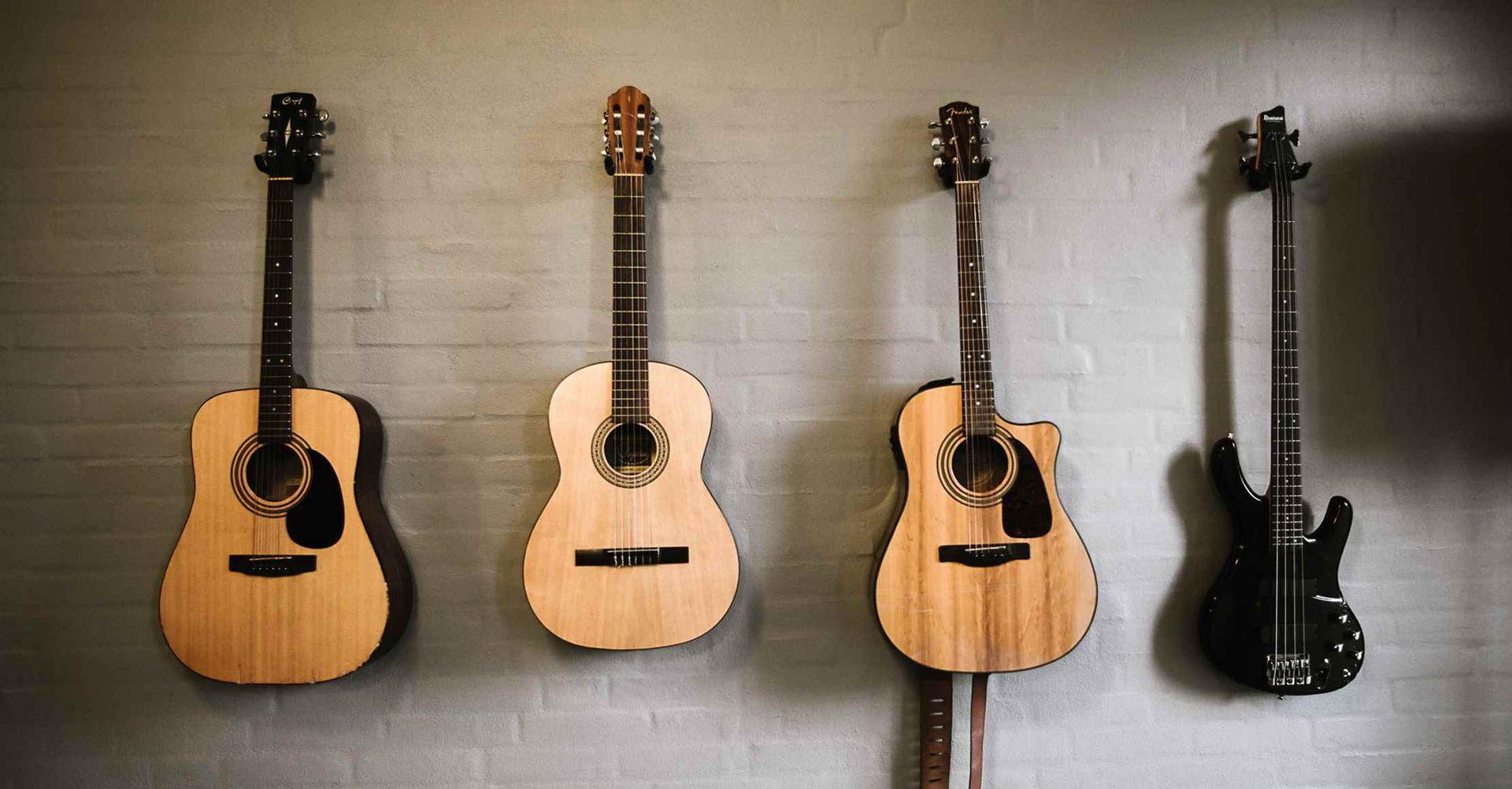 Fire guitarer i forskellige stilarter hænger på en struktureret væg.