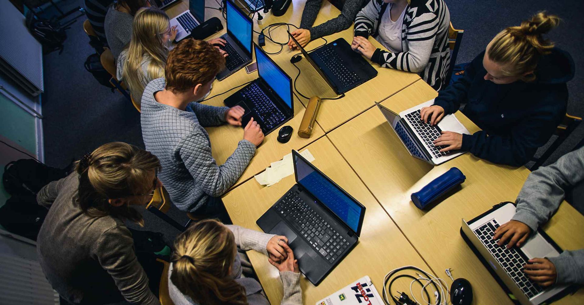 Folk arbejder på bærbare computere ved et rundt bord i et klasseværelse.