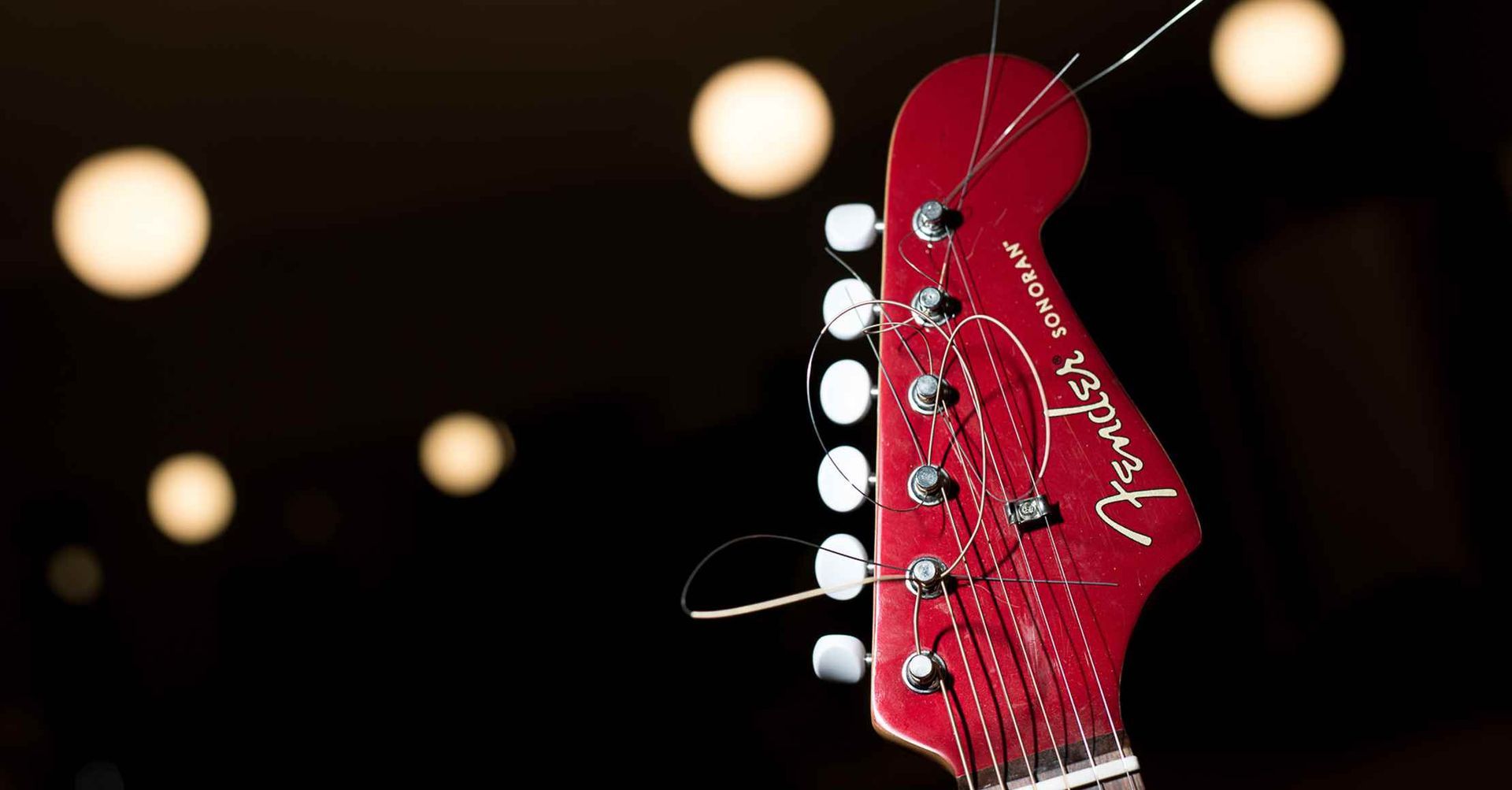 Rød Fender Mustang guitarhoved mod en sløret baggrund af lys.