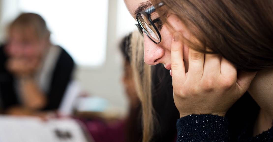 Kvinde med briller, hånden på ansigtet, kigger ned, i et møde.