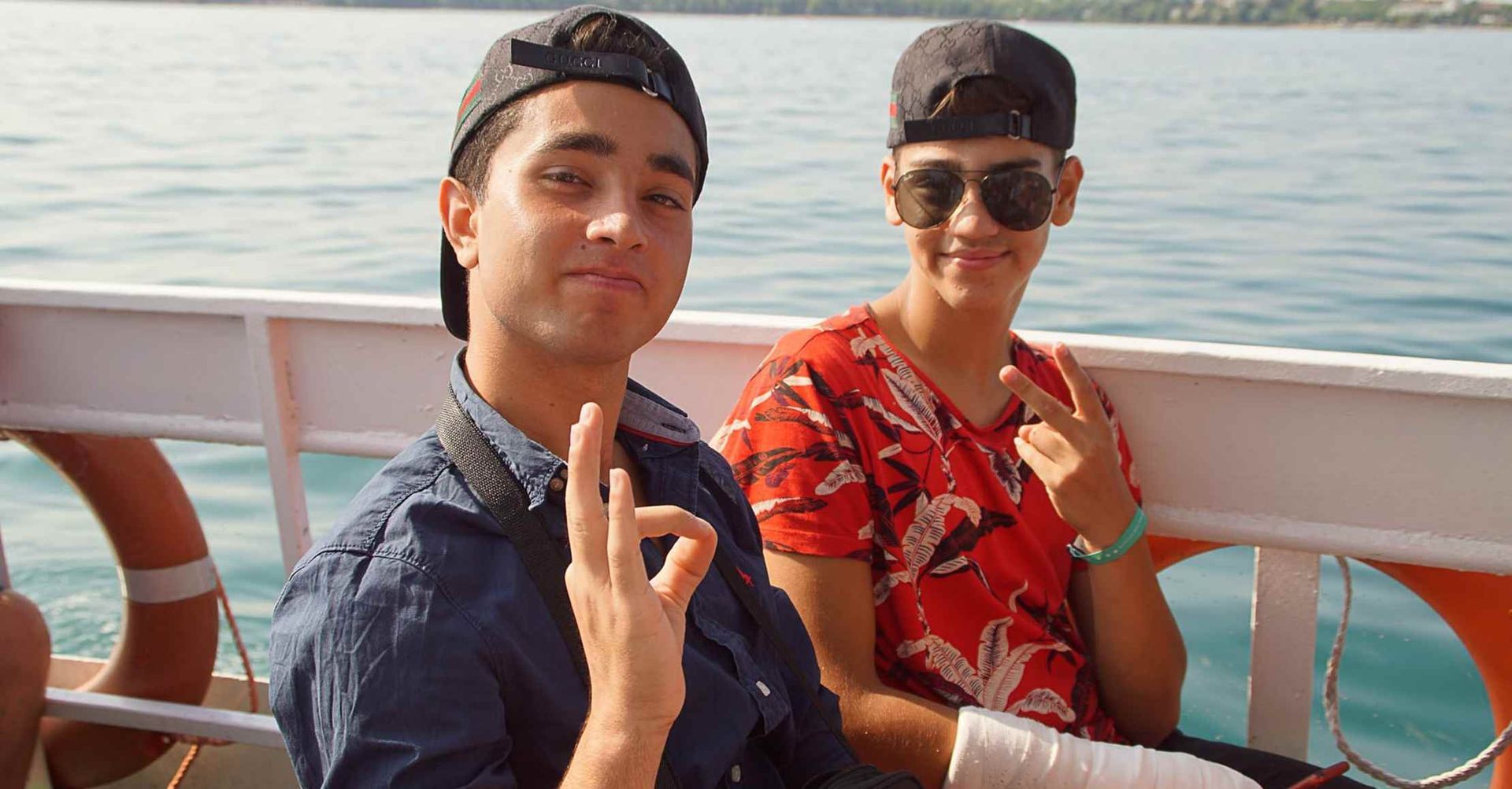 To personer på en båd med hatte og solbriller. Den ene laver en 