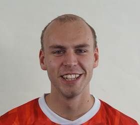 Mand med tyndt hår smiler, iført en orange og hvid skjorte, og ser på beskueren.