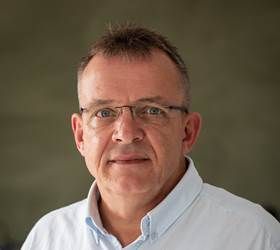 Mand med briller og lyseblå skjorte, smilende og kigger ind i kameraet.