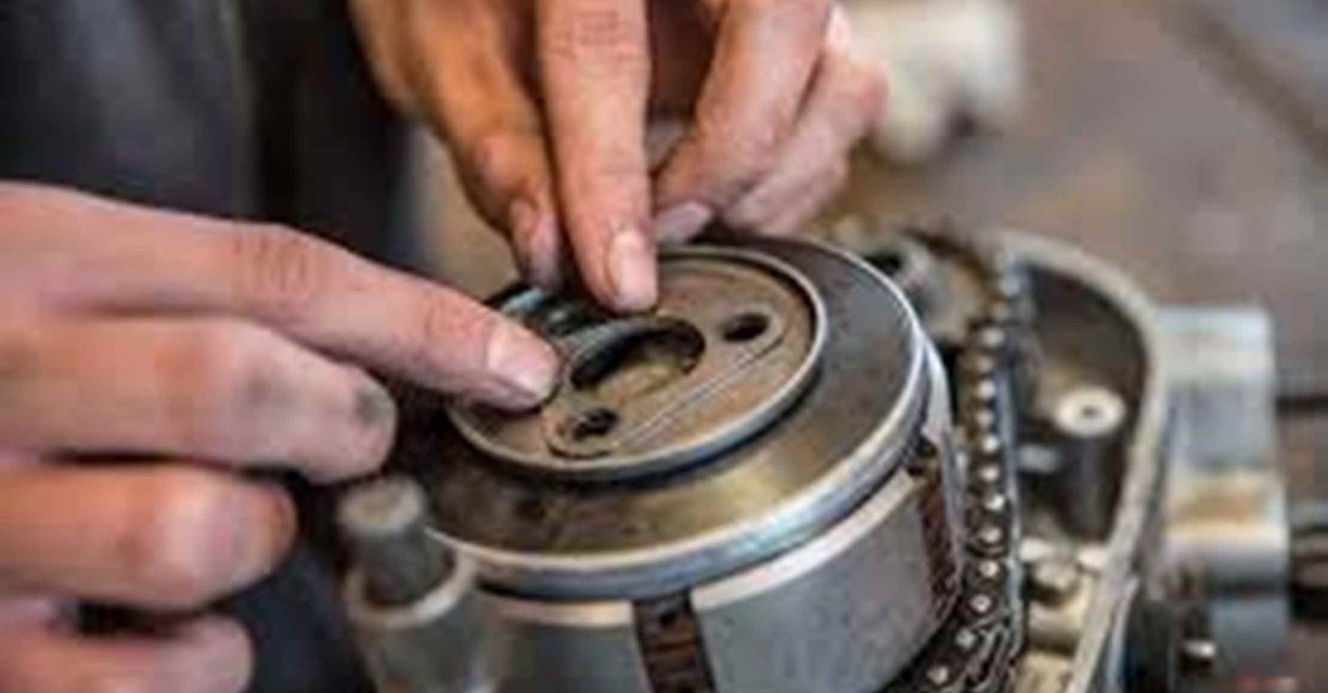 Hænder arbejder på en motorcykelmotor og placerer en pakning på en cirkulær komponent.