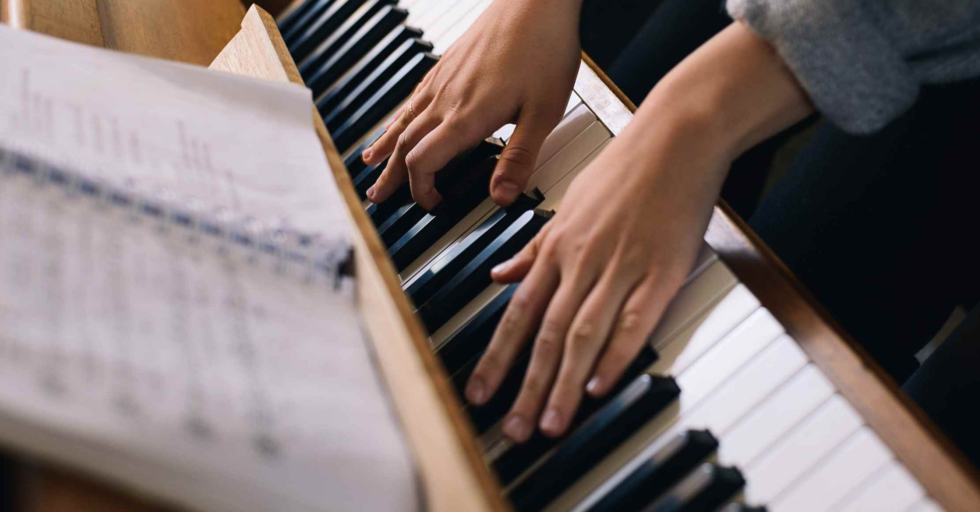Hænder spiller på et klaver, noder synlige.