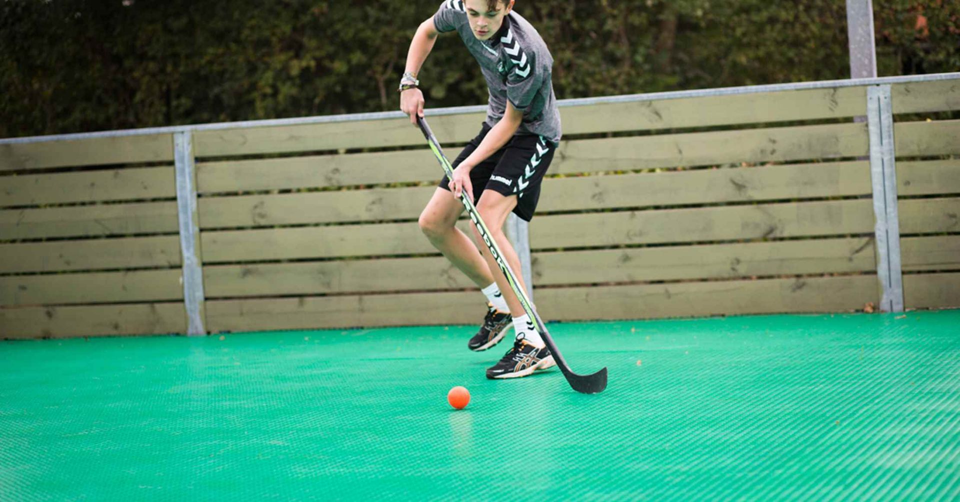 En person, der spiller gulvhockey på en grøn bane, holder en stav og en orange bold.