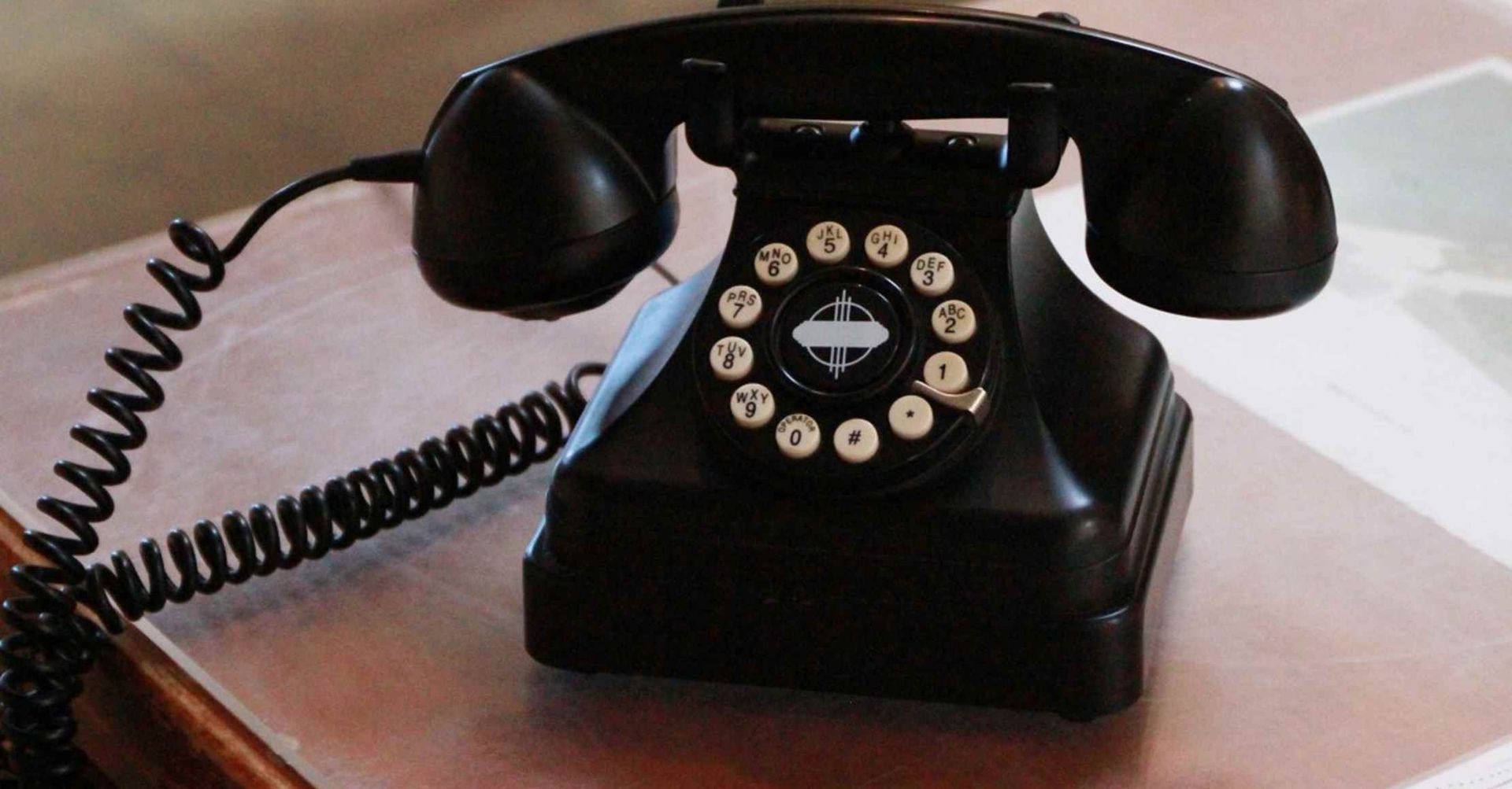 Sort vintage drejetelefon på et skrivebord, røret taget af, spiralledning synlig.