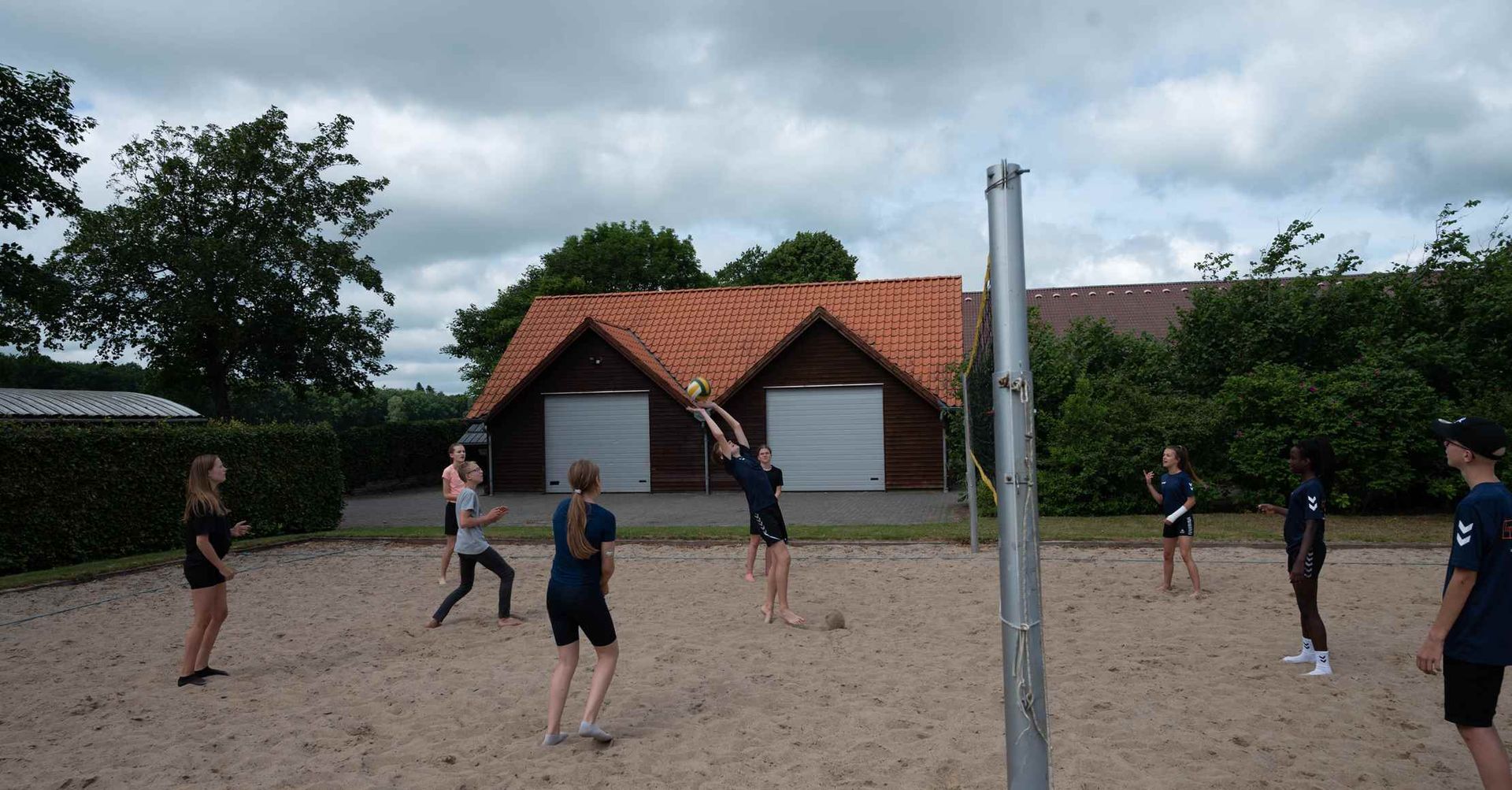 Folk spiller volleyball på en sandbane; én person hopper for at ramme bolden.