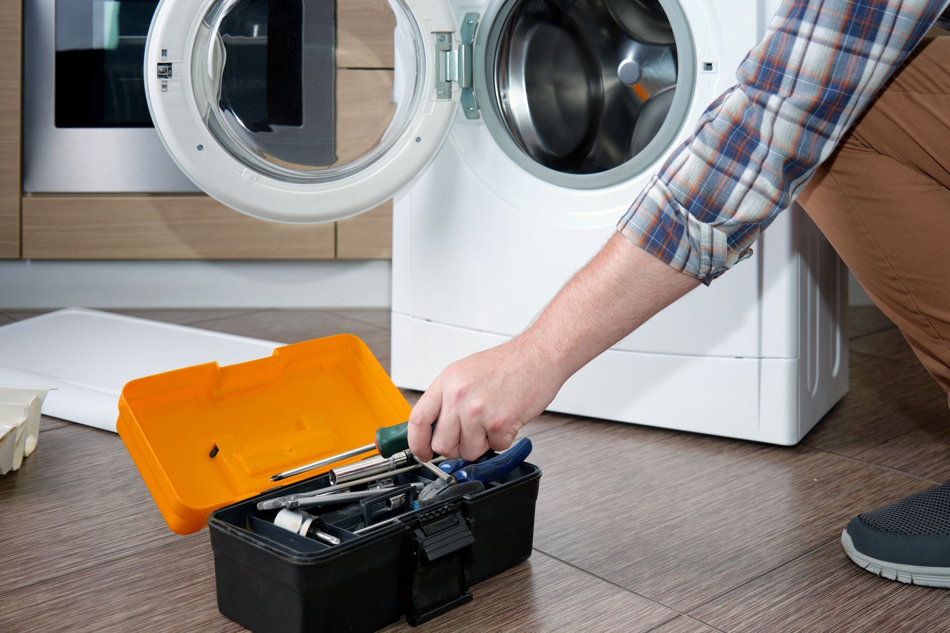 A man is repairing a washing machine with a toolbox filled with tools.
