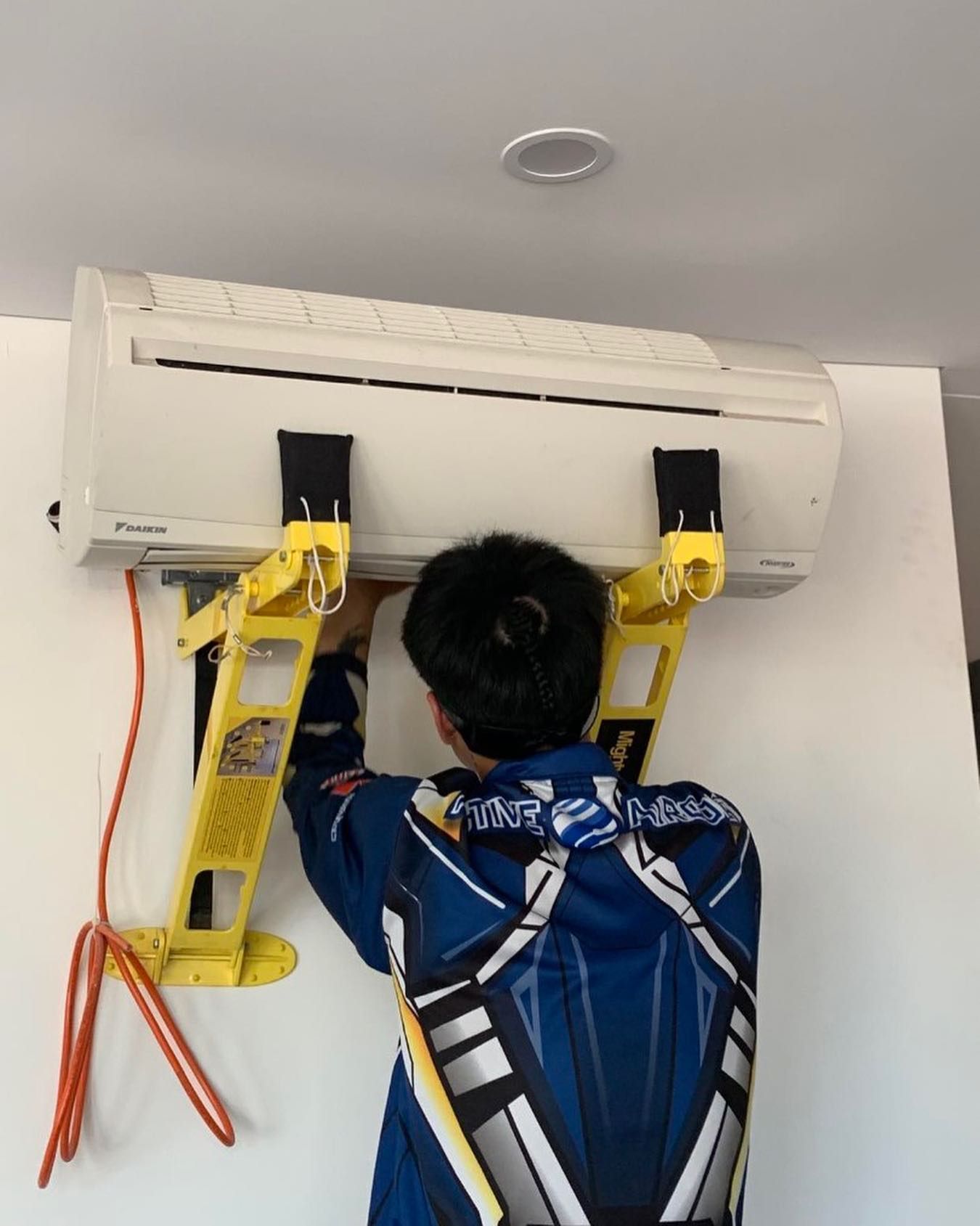 Person installing an air conditioner unit on a wall, using yellow support brackets. — Active Airconz in Perth, WA