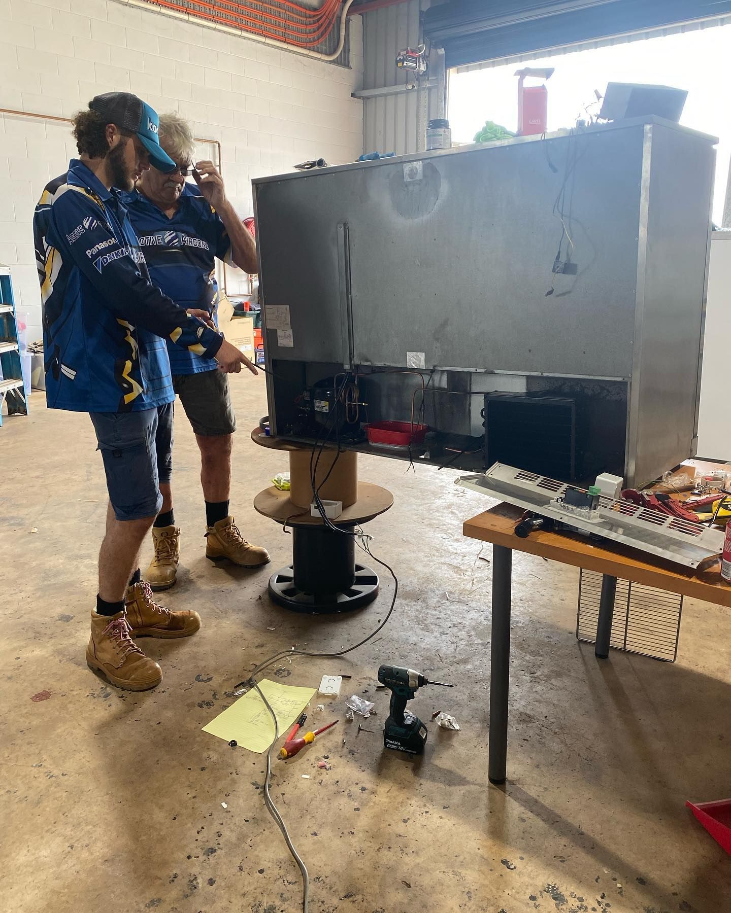 Two men working on a large metal appliance in a workshop. One points at the appliance. — Active Airconz in Mackay, QLD