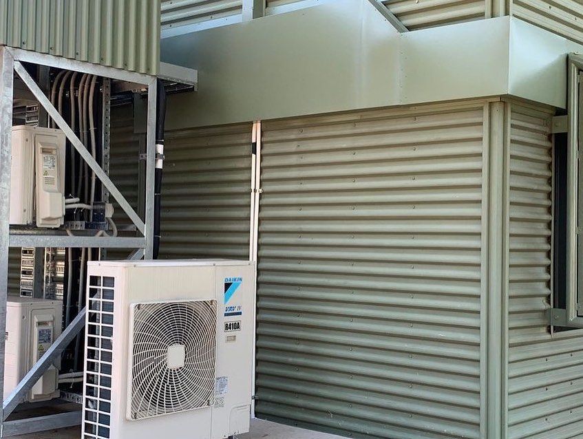Outdoor HVAC unit next to corrugated metal building, with wiring and ductwork visible. — Active Airconz in Gold Coast, QLD