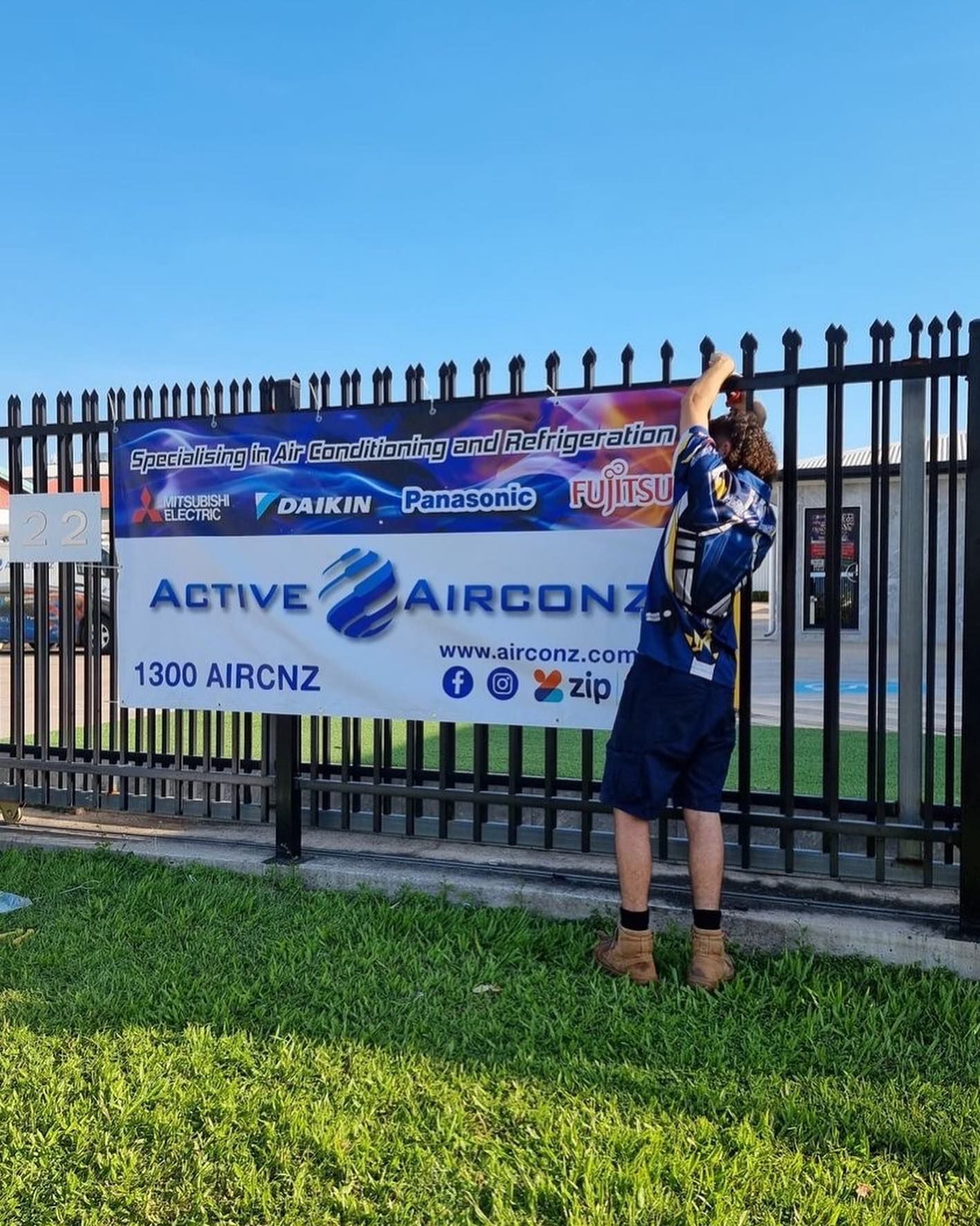 A Person Hanging a Banner for Active Airconz on a Black Metal Fence, Grass Foreground — Active Airconz in Nhulunbuy, NT