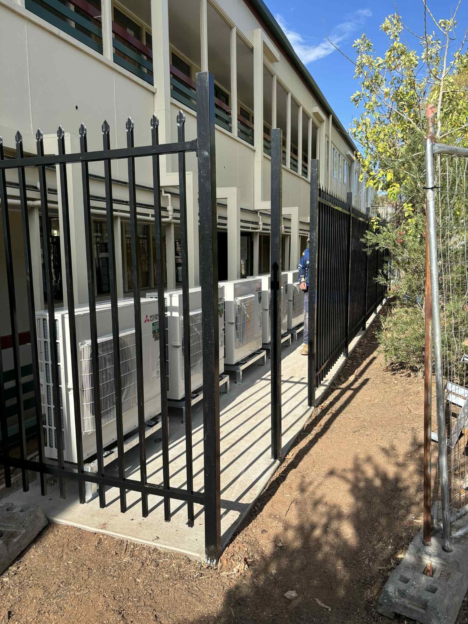 Black fence encloses air conditioning units along the side of a building with a balcony. — Active Airconz in Perth, WA