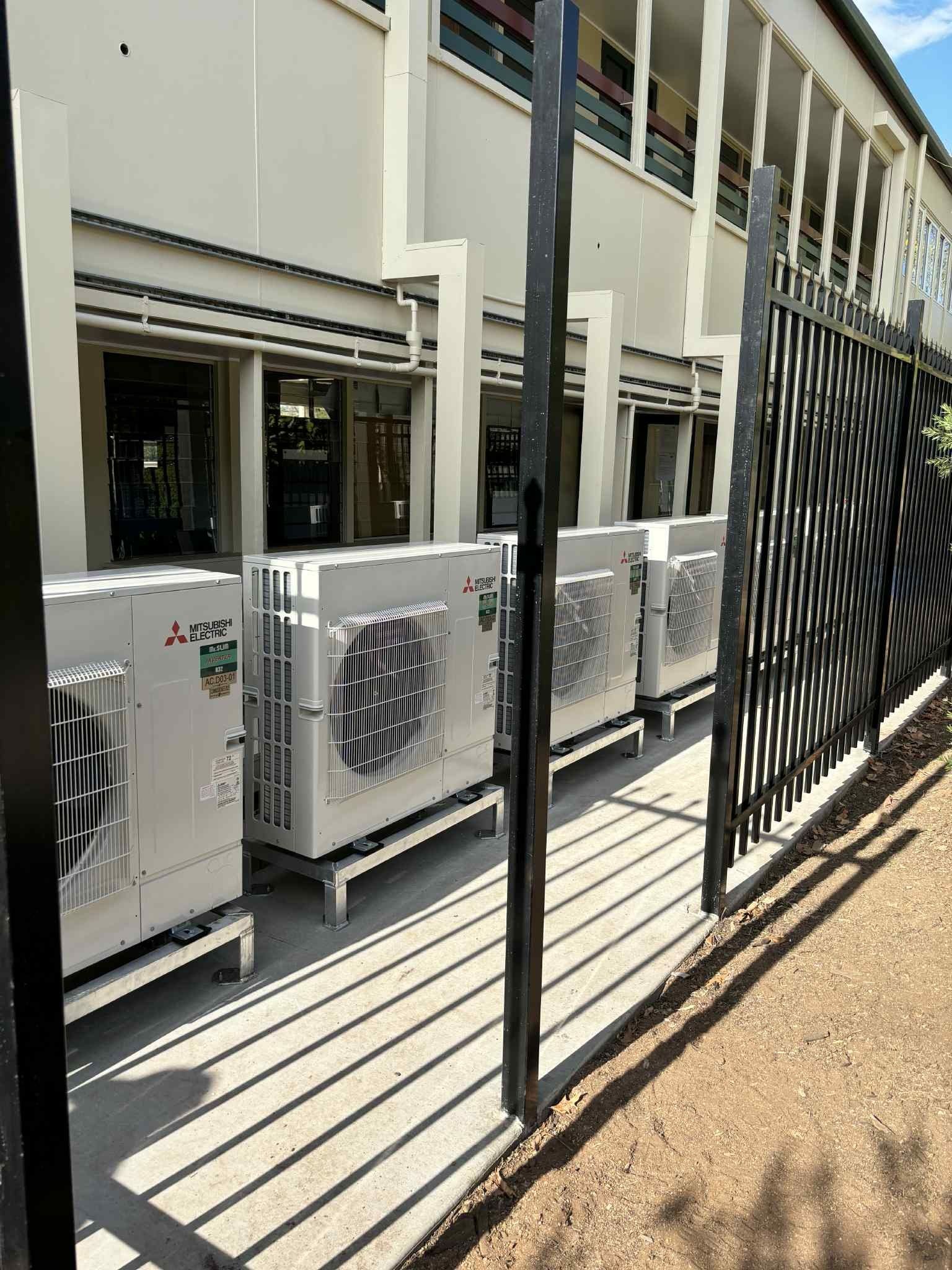 White AC Units Lined Up Outside a Building Behind a Black Fence — Active Airconz in Sunshine Coast, QLD