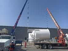 Una grúa levanta un gran tanque blanco en un camión de plataforma.
