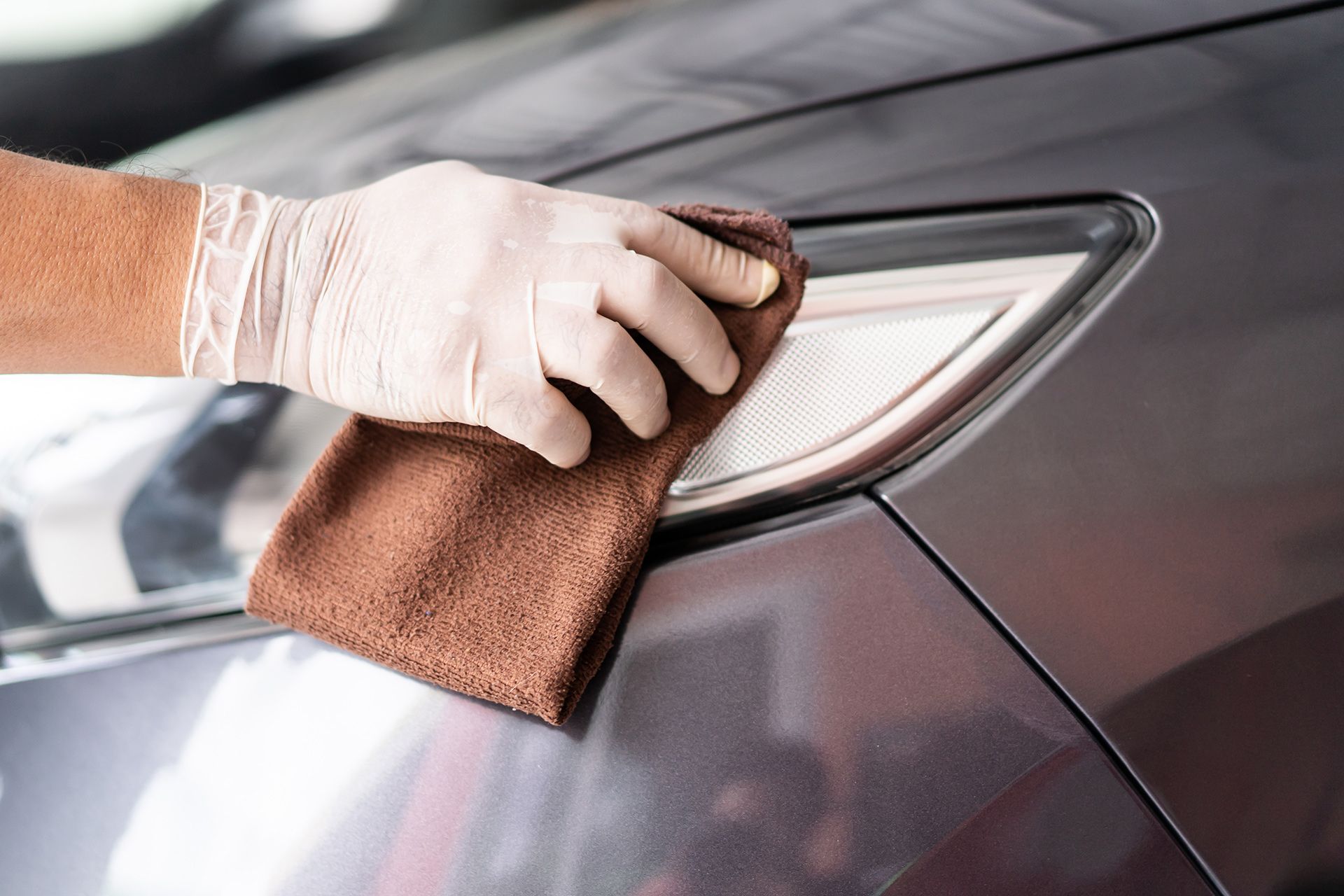 A person is cleaning a car with a towel and gloves.