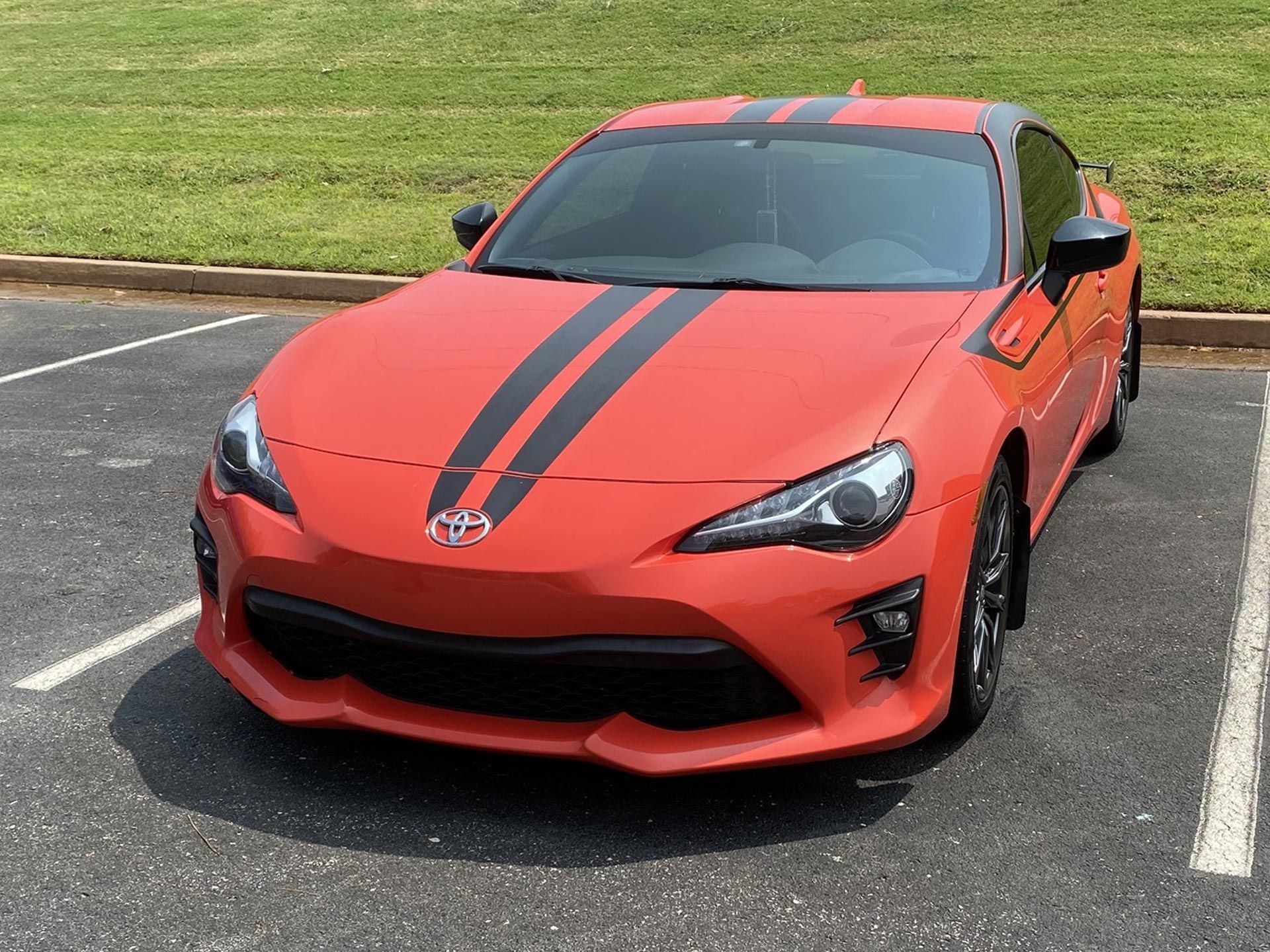 A red sports car with black stripes is parked in a parking lot being cleaned