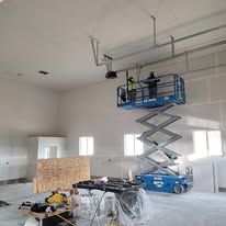 Two men are working on a scissor lift in a large room.