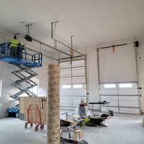 A man is standing on a scissor lift in a garage.