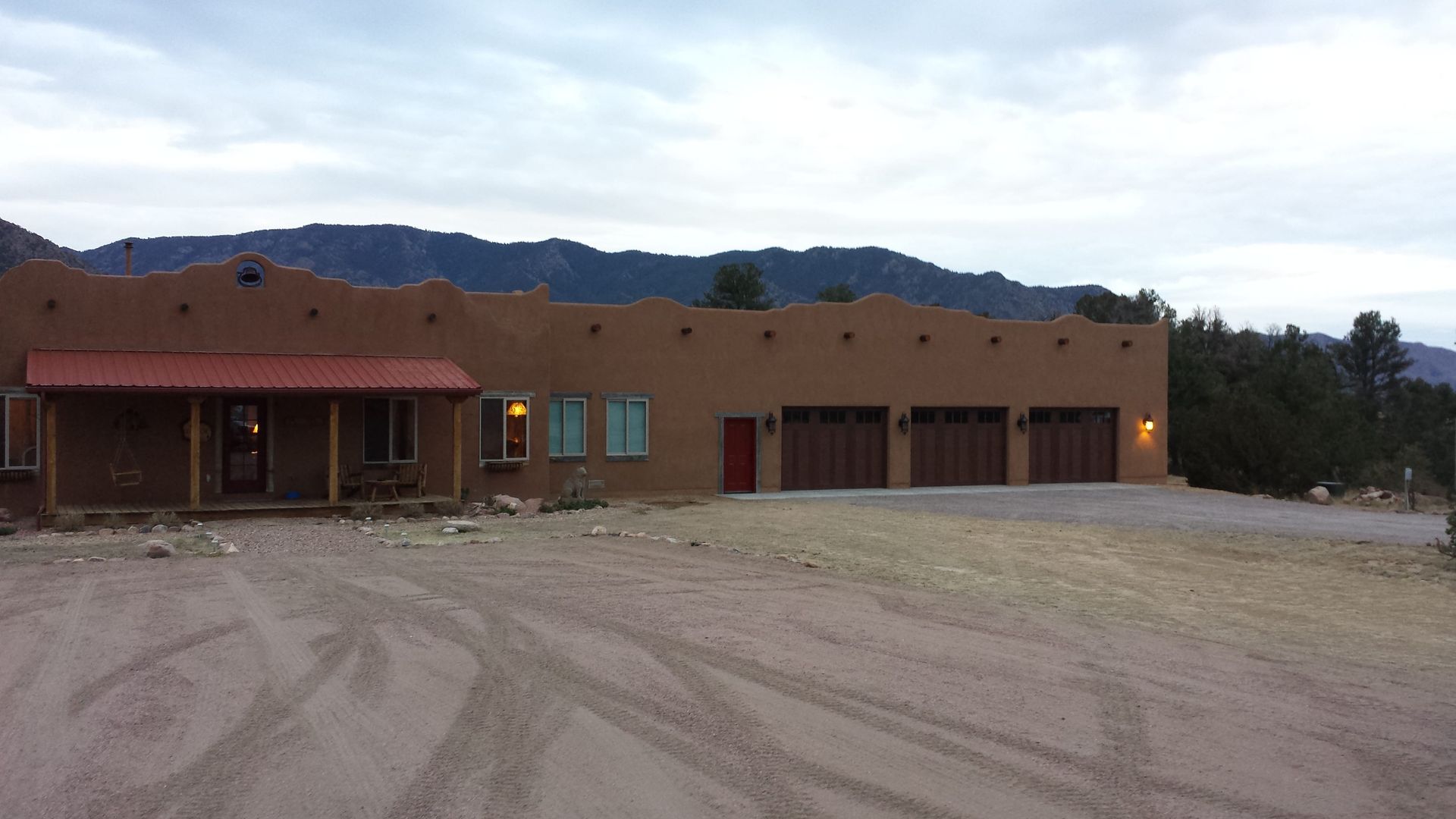 A large adobe house with three garage doors and a porch with mountains in the background.