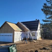 A man is standing in front of a house under construction with solar panels on the roof.