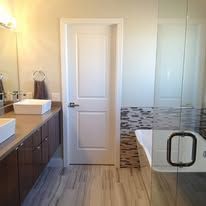 A bathroom with a tub , sink , mirror and door.