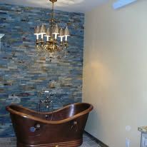 A bathroom with a copper bathtub and a brick wall.