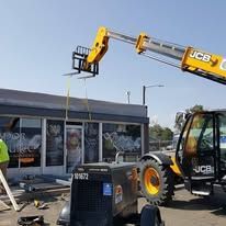 A tractor with a crane attached to it is working on a building.