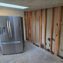 A stainless steel refrigerator is sitting in a room with a wooden wall.