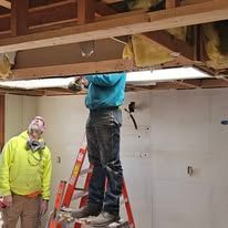 A man is standing on a ladder working on a ceiling.