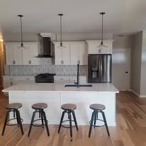 A kitchen with white cabinets , stools , a refrigerator and a sink.