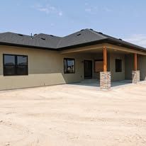 A house with a porch and a lot of windows is sitting on top of a dirt field.