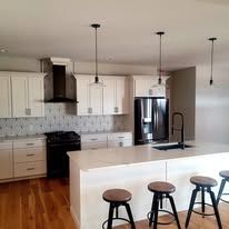 A kitchen with white cabinets , stainless steel appliances , a large island , and stools.