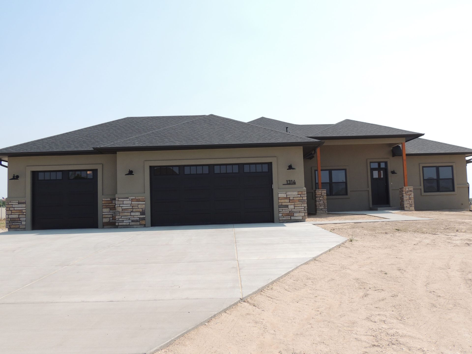 A large house with two black garage doors and a concrete driveway.