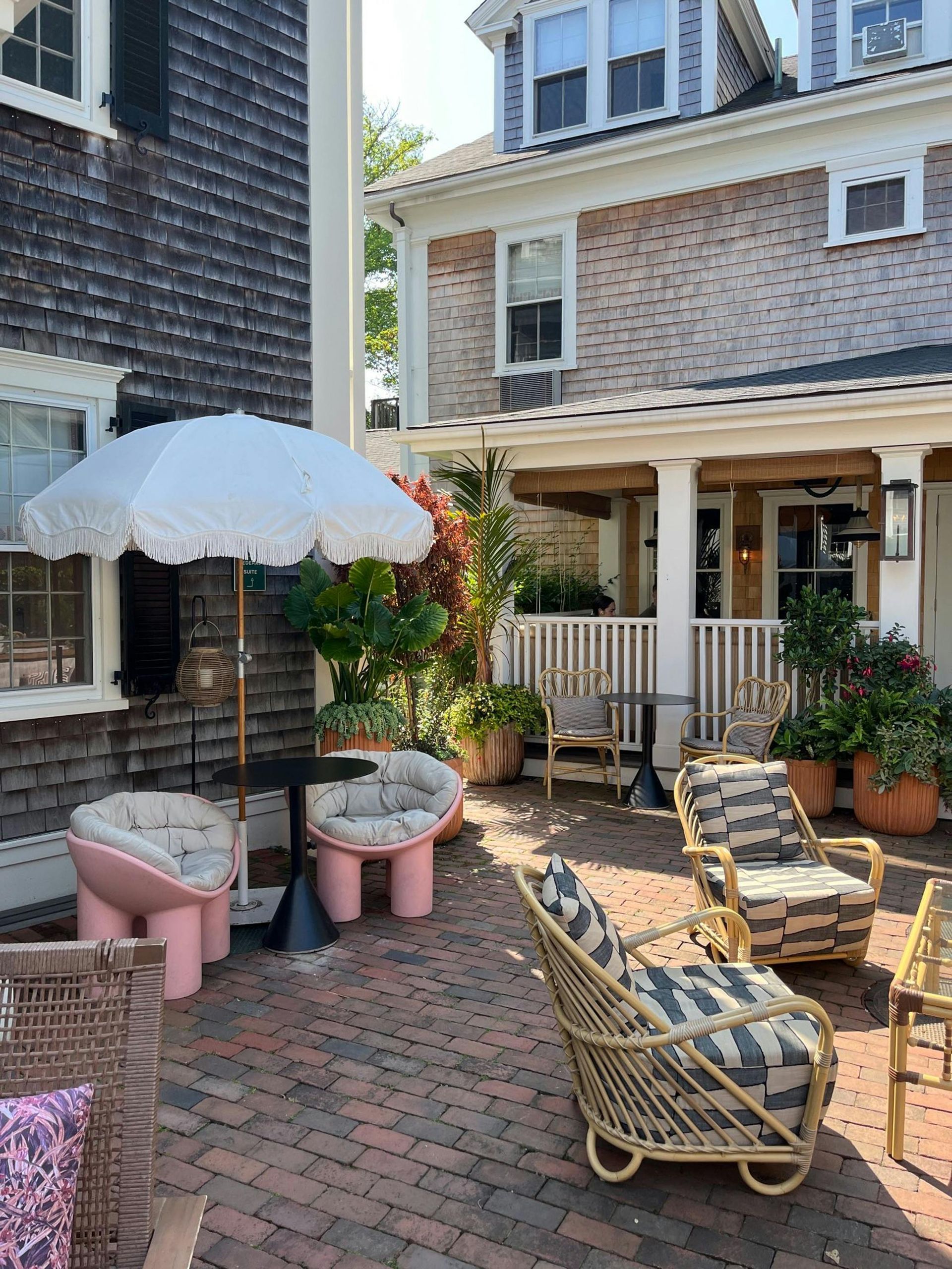 Outdoor patio seating area with umbrellas and various chairs on a brick surface.