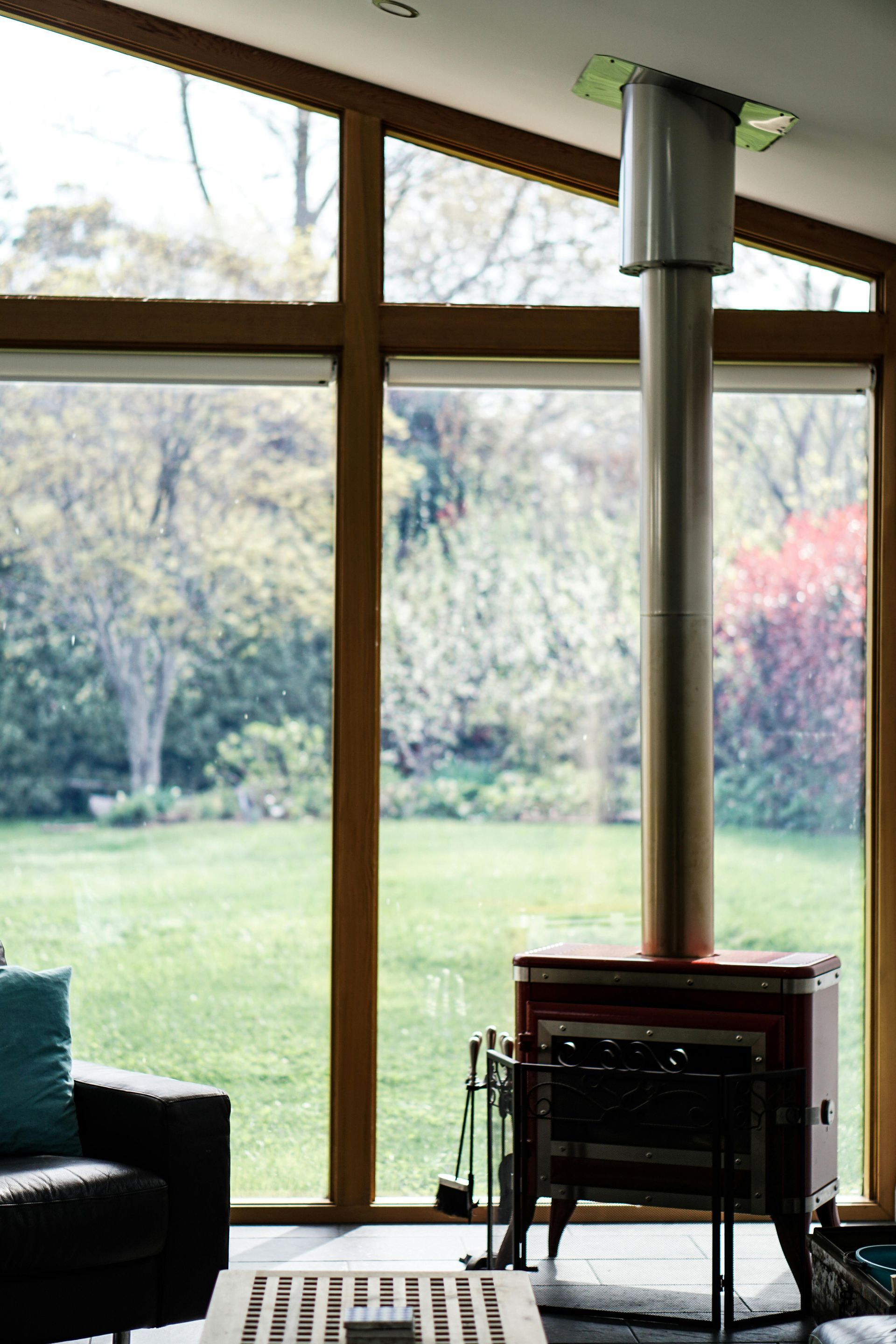Wood stove with chimney, in front of large window overlooking a yard.