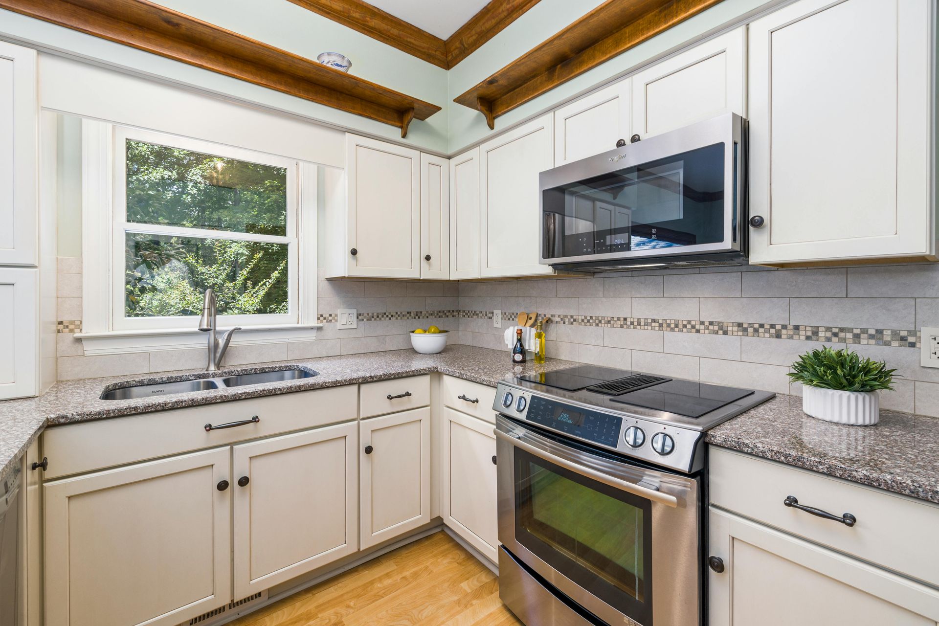 White kitchen with stainless steel appliances, granite countertops, and a window.