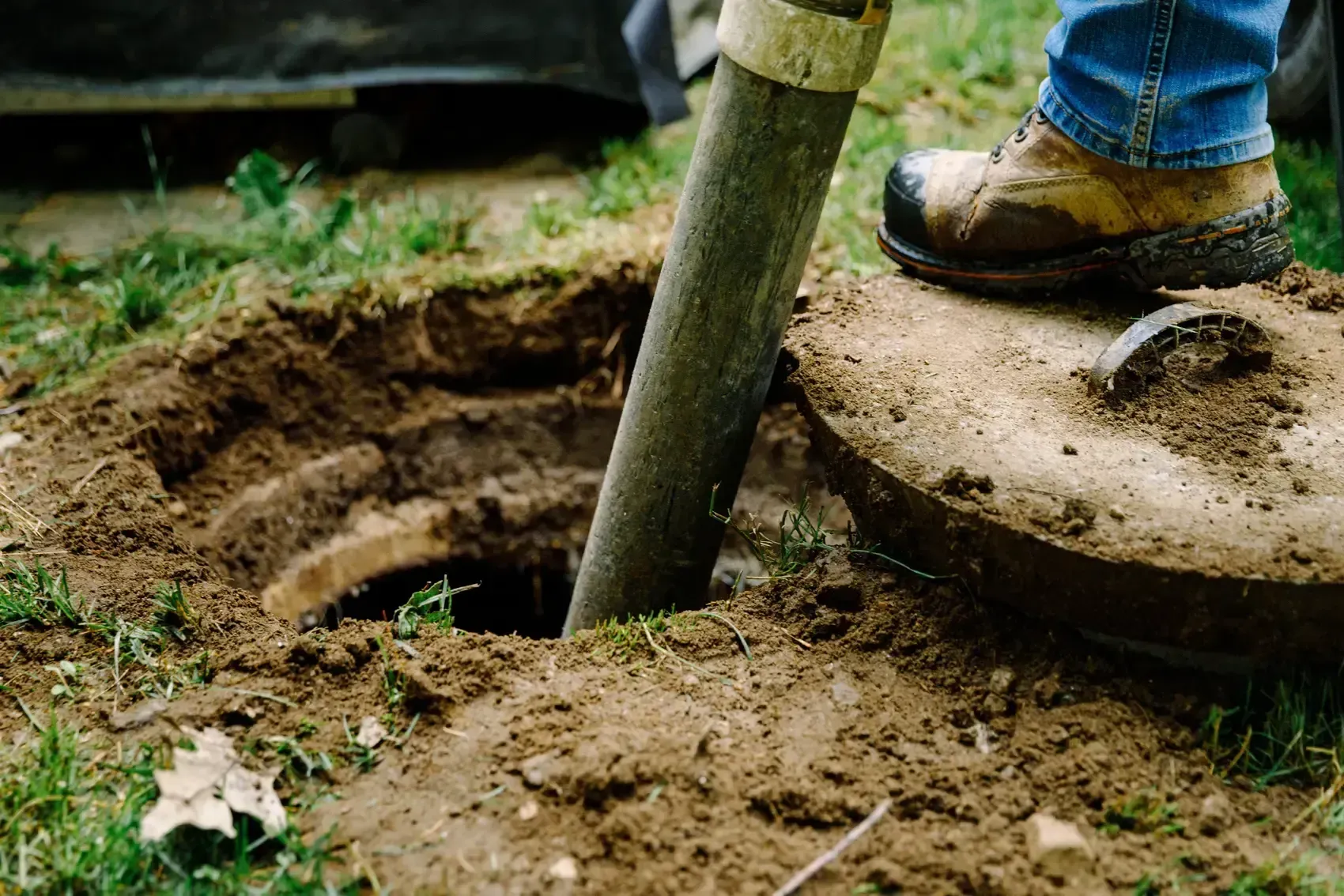 A person is digging a hole in the ground to install a septic tank.