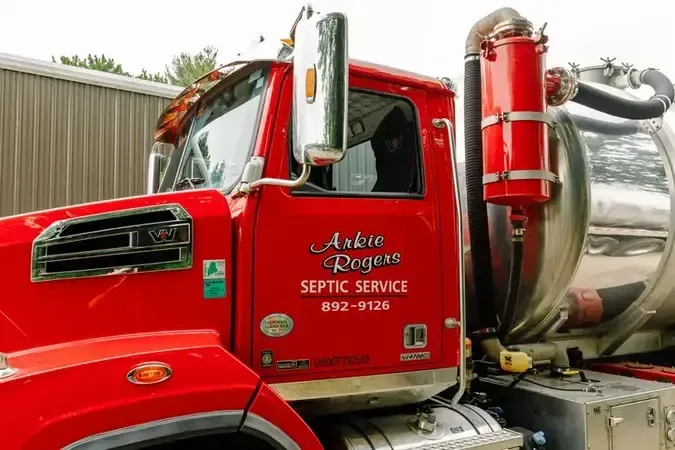 A red Arkie Rogers  septic service truck is parked in front of a building