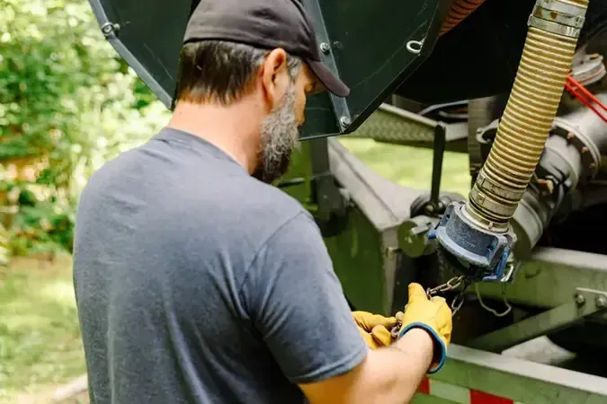 A man is working on a truck with a hose to pump a septic system.