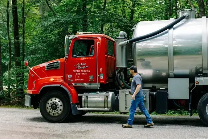 A man is walking next to a septic pumping vacuum truck.