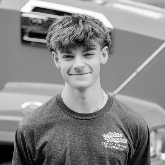 A young man wearing a t-shirt is smiling in front of a car. He is Arkie Rogers Emplyee.