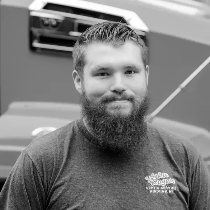 A man with a beard is standing in front of a truck in a black and white photo. Arkie Rogers Employee