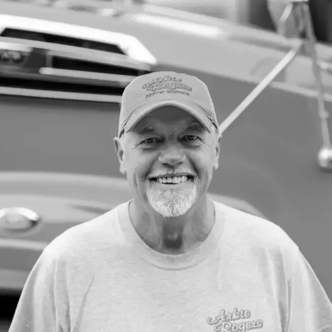 A man with a beard is wearing a hat and smiling in front of a boat. Arkie Rogers Employee