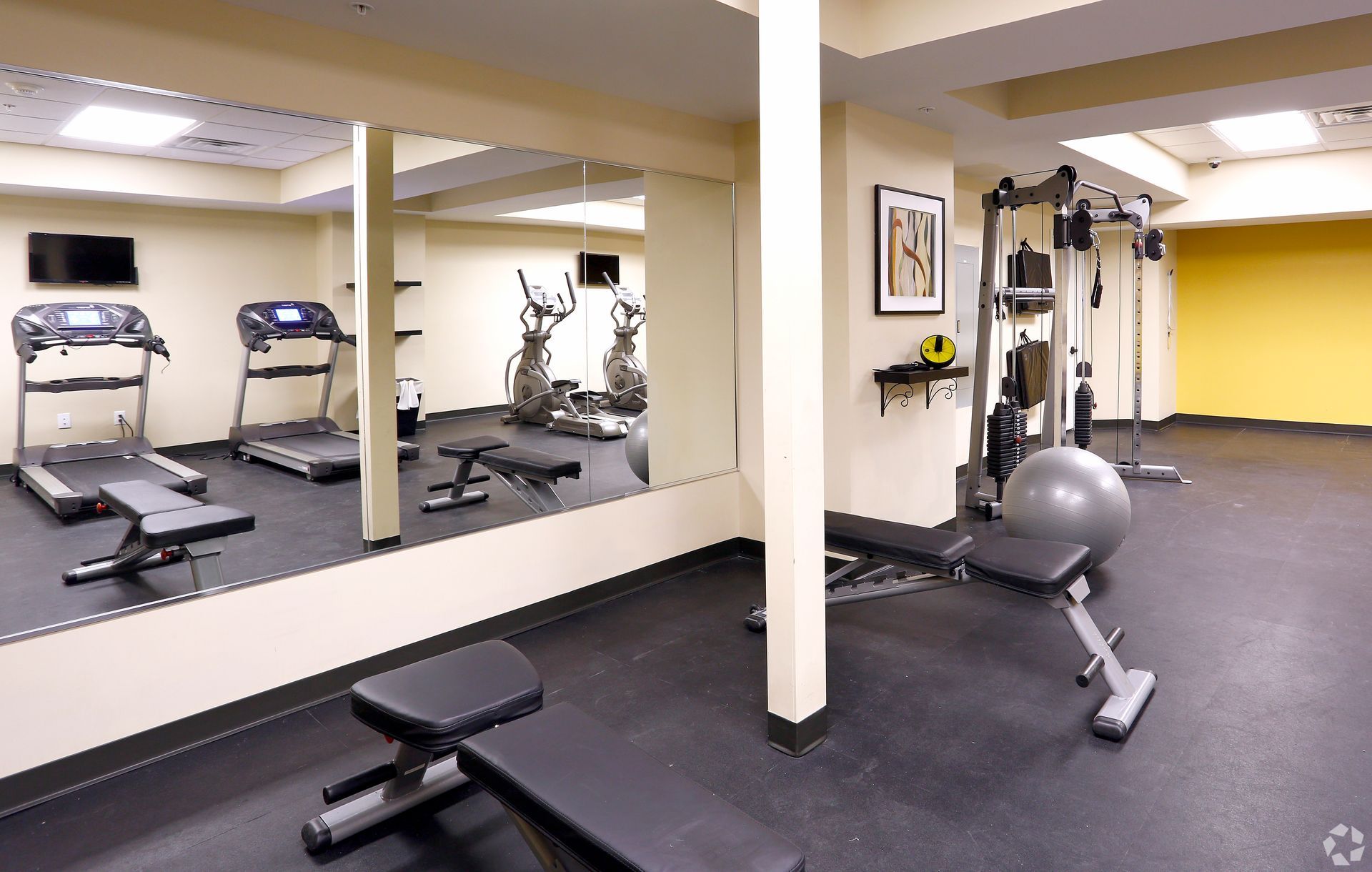 A gym with treadmills , exercise bikes , a bench and a large mirror.