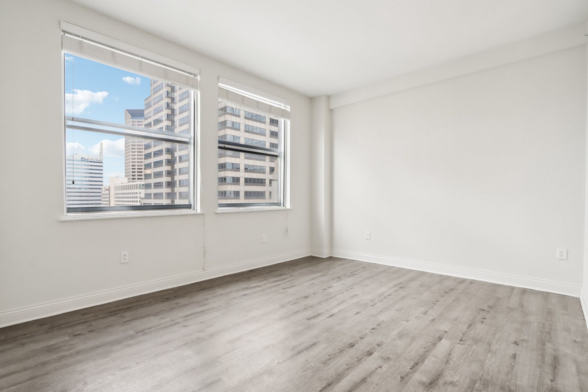 An empty room with hardwood floors and two windows.